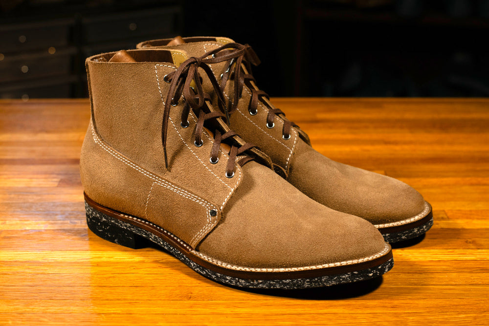Pair of brown suede boots on a wooden surface with a dark background