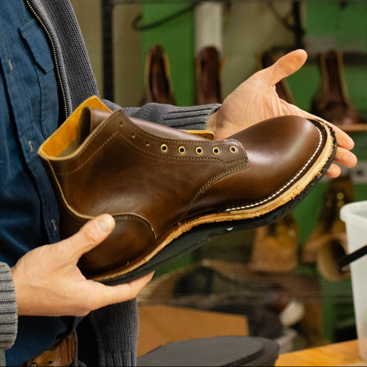 Man holding a brown leather shoe in a workshop setting