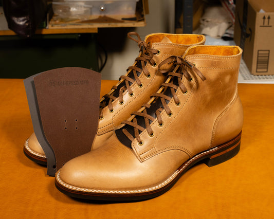 Pair of tan leather boots on a wooden surface with a blurred background