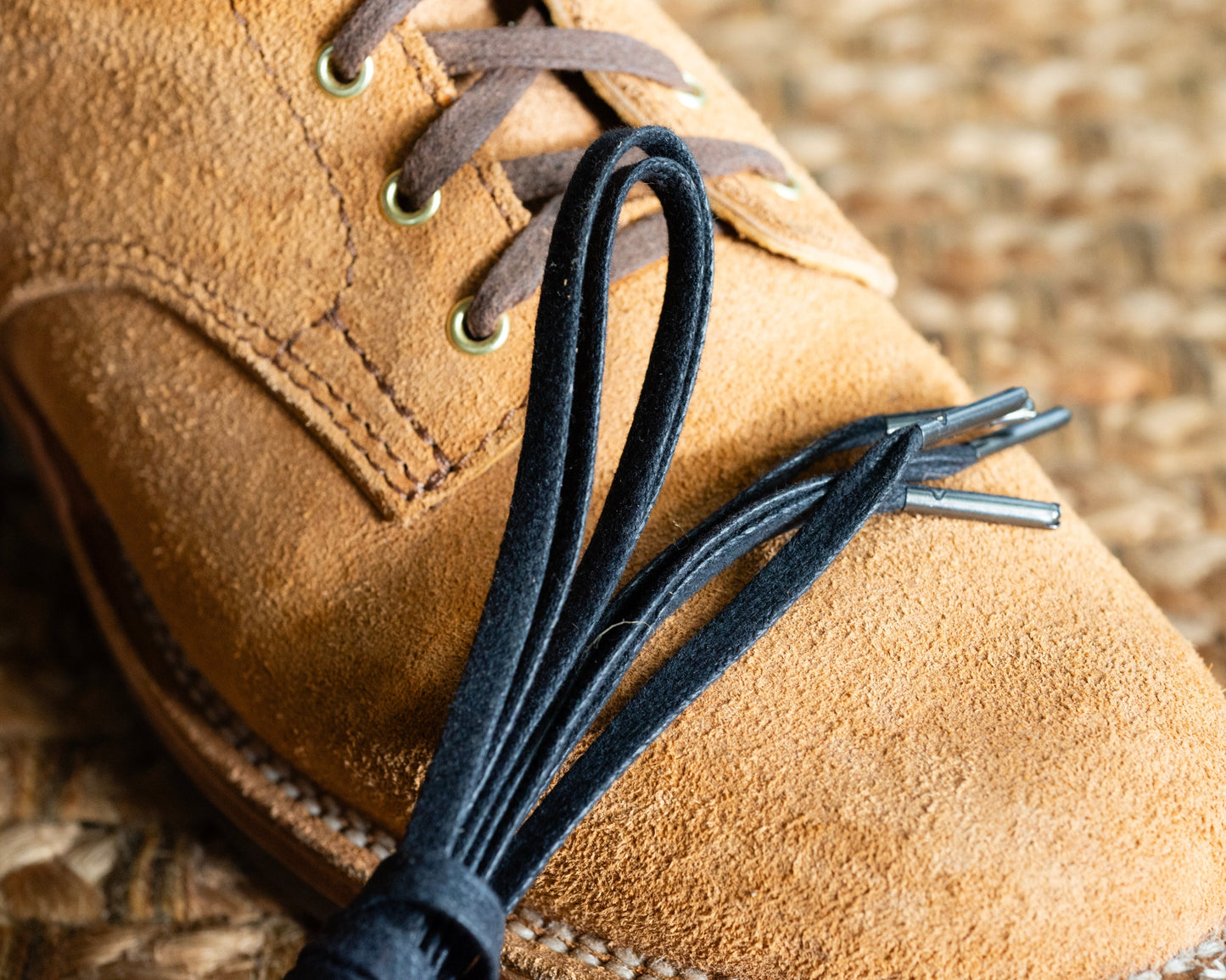 Close-up of a brown suede shoe with black laces on a textured surface