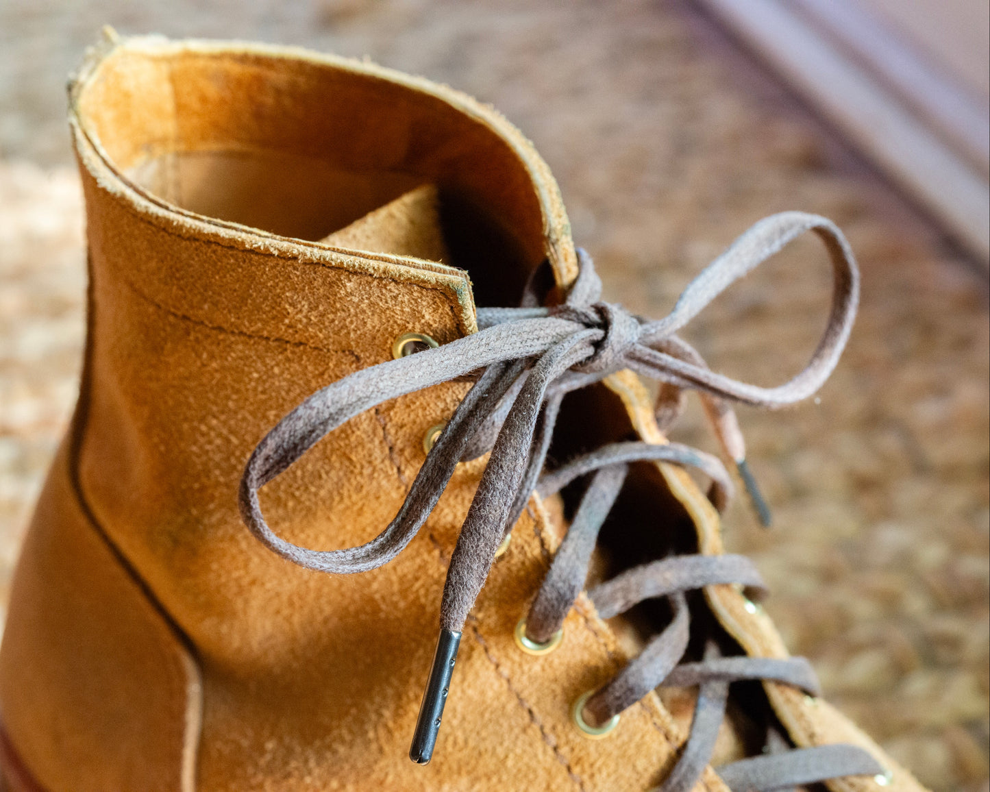 A pair of brown flat waxed cotton laces with eyelets, displayed on a textured background.